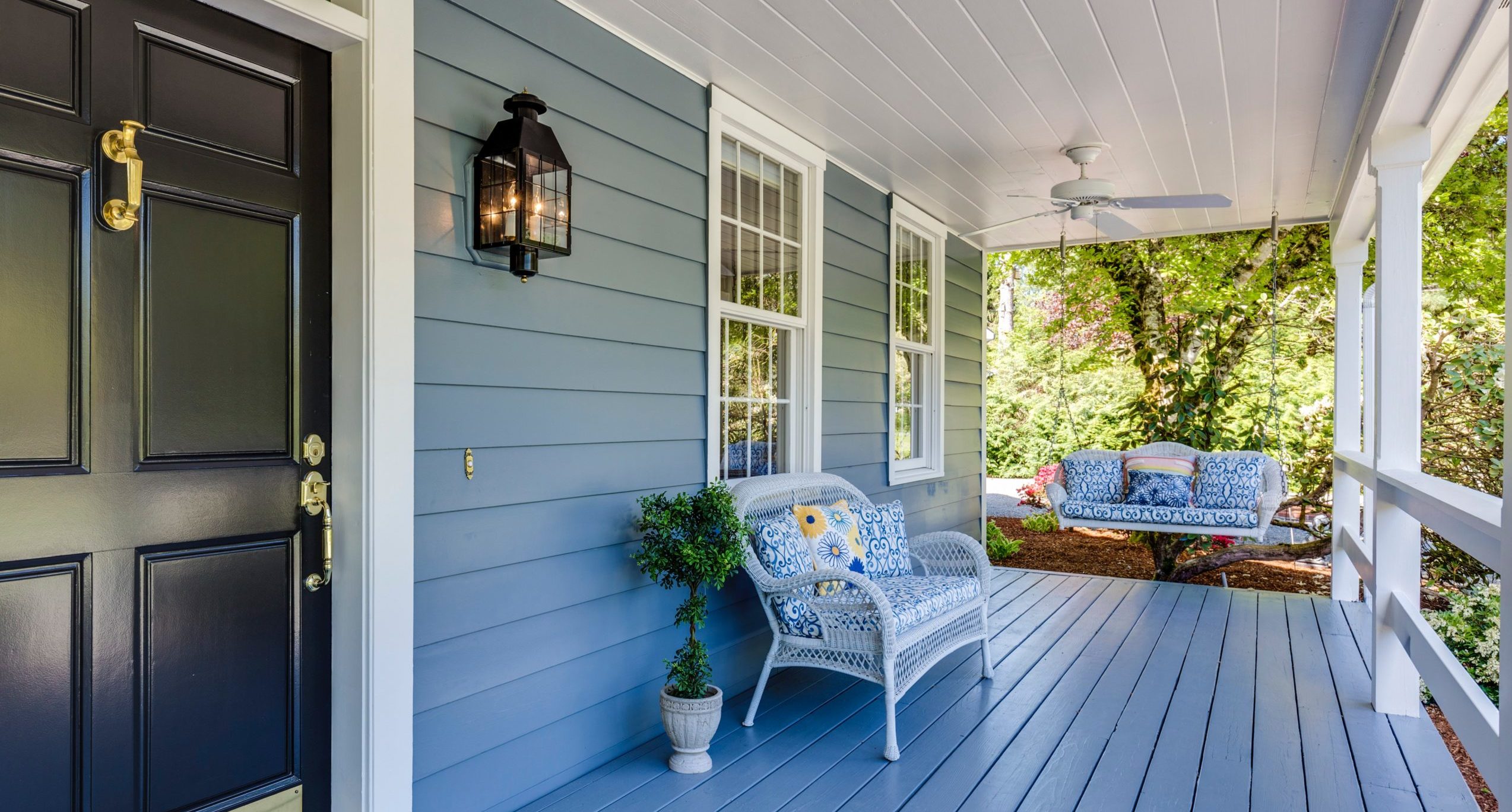 light blue porch wih white wicker loveseat and porch swing with tree in background