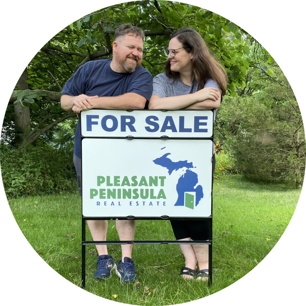 Amy and William standing behind a pleasant peninsula for sale sign in a grassy yard in ann arbor MI